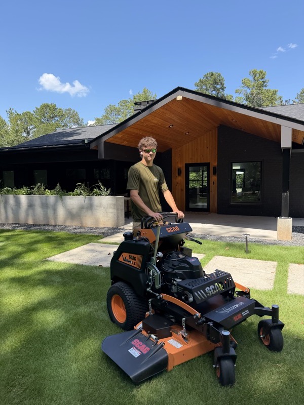 Noah with the stand-on mower in front of a modern home