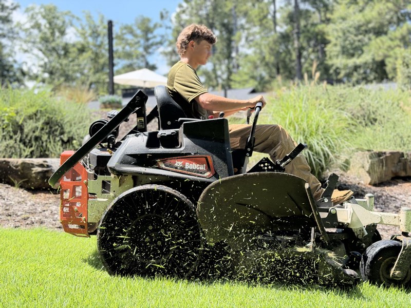 Noah mowing beside a landscaped bed on a zero-turn mower