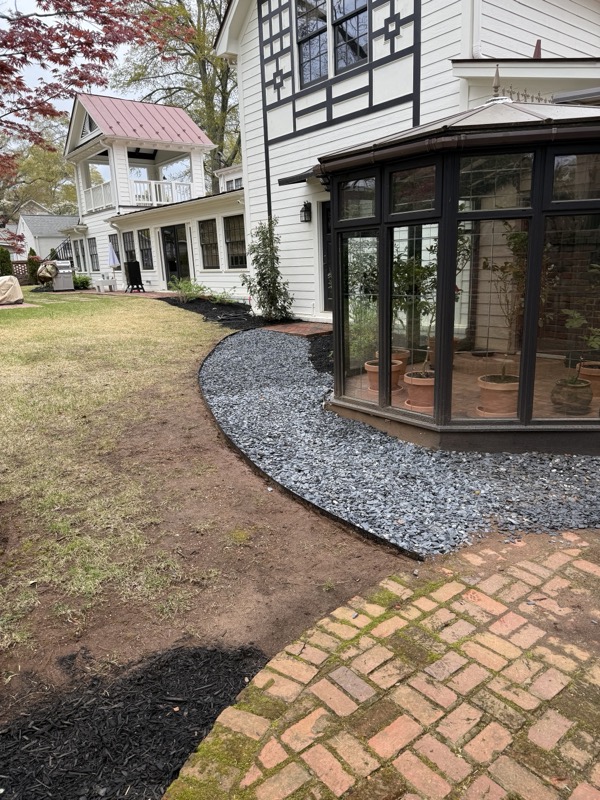 Black mulch bed edged with slate gravel along a sunroom and brick patio